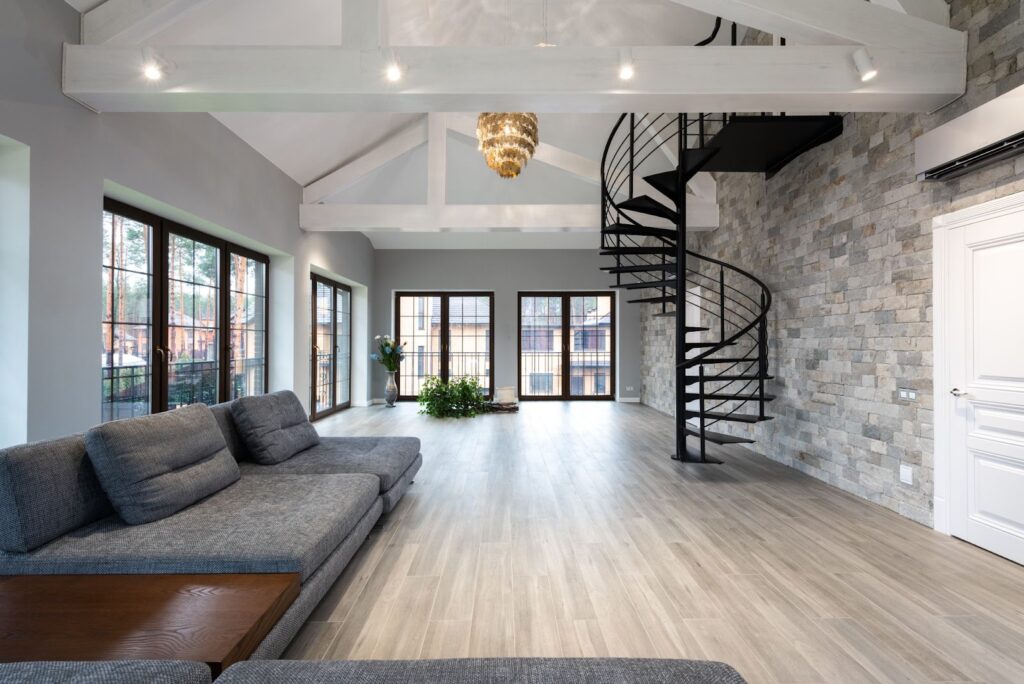 Open concept rec room in luxury home with a grey sectional sofa, and winding wrought iron staircase.